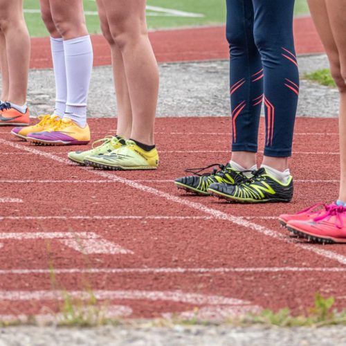 Group of runners preparing to start a race with vibrant footwear on a track.